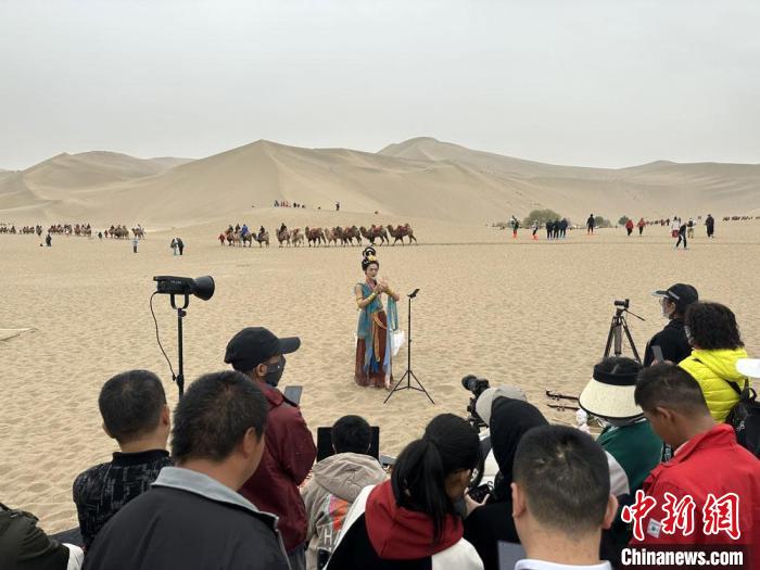 圖為2023年4月底，敦煌大漠“逐舞者”奧楠在鳴沙山月牙泉景區(qū)視頻直播，吸引游人圍觀。　馮志軍 攝